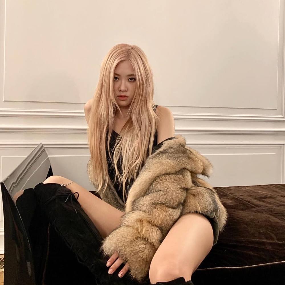 Rosé (BLACKPINK) mang áo khoác lông đang ngồi trên ghế.