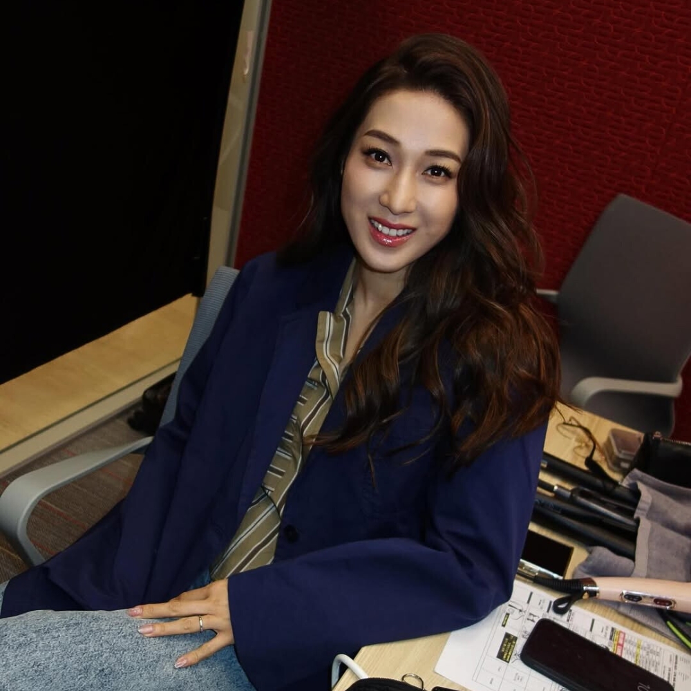 Chung Gia Hân mang áo blazer xanh dương đậm và xõa tóc xoăn nhẹ.