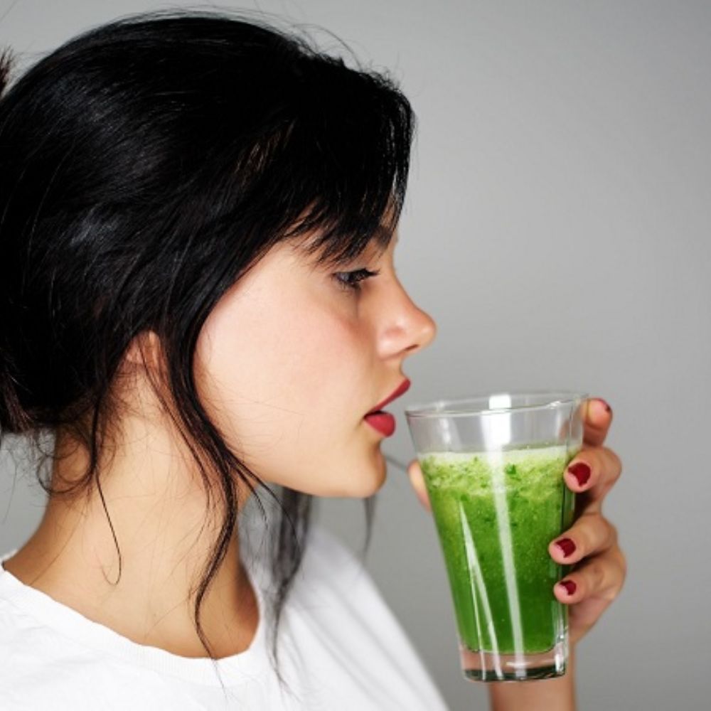 Người phụ nữ trẻ uống một ly nước lá thảo mộc xanh – gợi ý cách sử dụng trà lá ổi để chăm sóc sức khỏe và làn da từ bên trong.