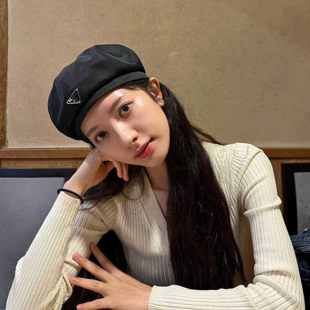 Bona đội mũ ngồi chống tay lên gò má