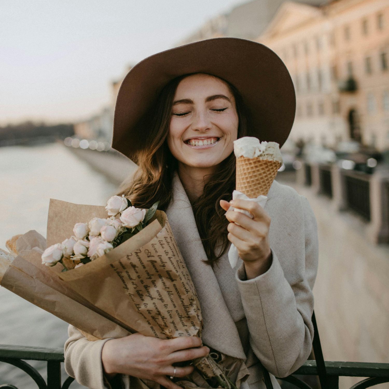 Cô gái mặc măng tô đội nón rộng vành có dấu hiệu ôm bó hoa tươi cười ăn kem ở trên cầu