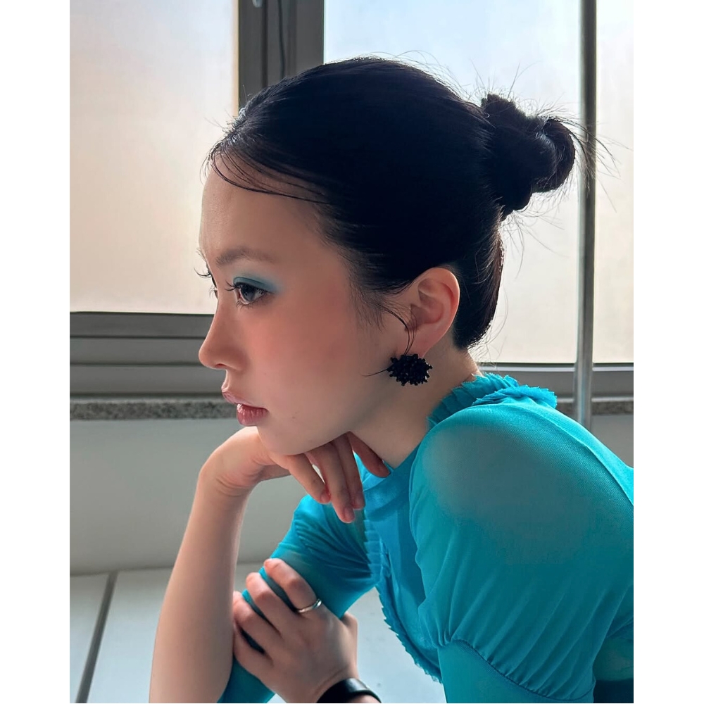 Cô gái mang áo xanh, trang điểm mắt xanh ngồi chống tay lên cằm