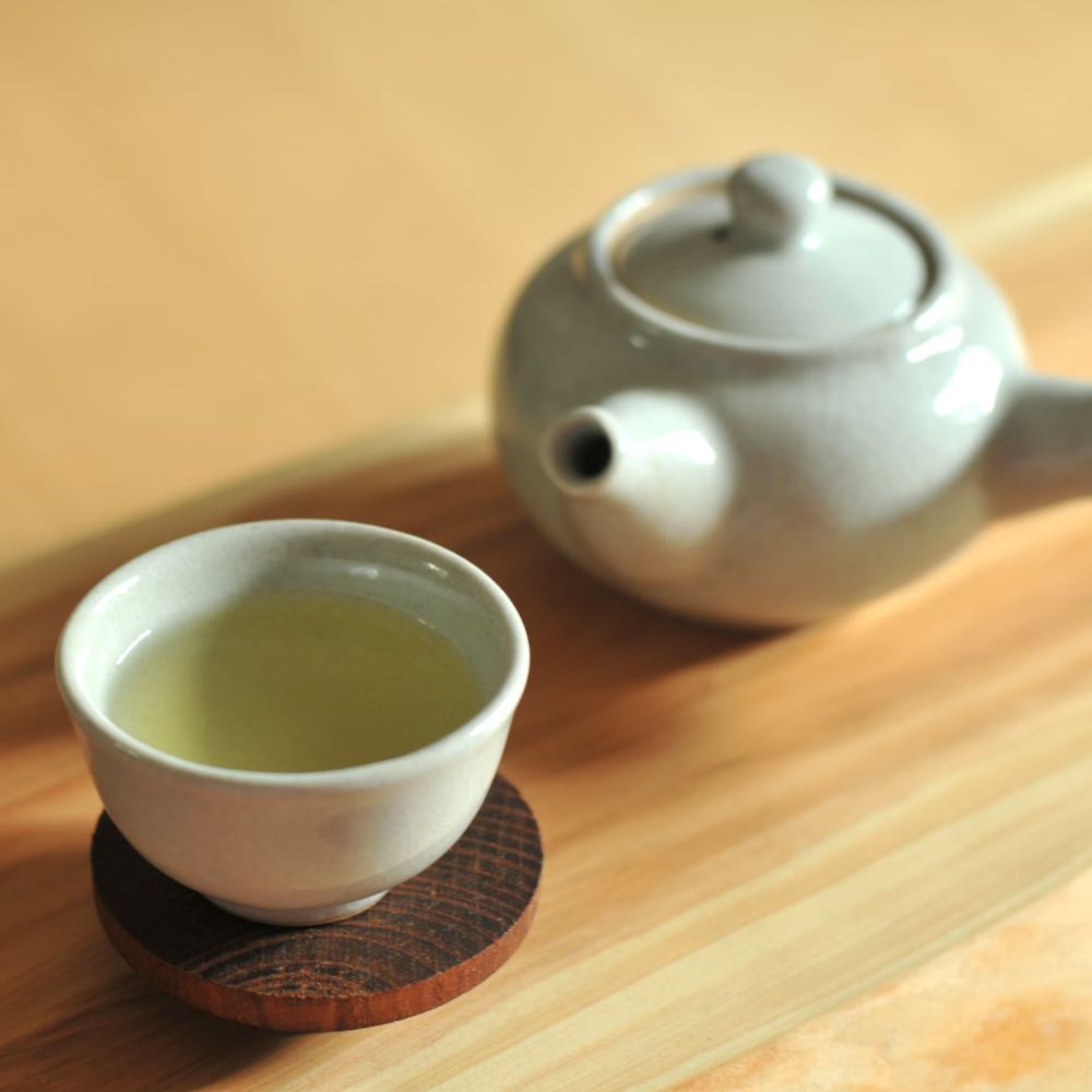 Tách trà xanh và ấm trà nhỏ bên cạnh.