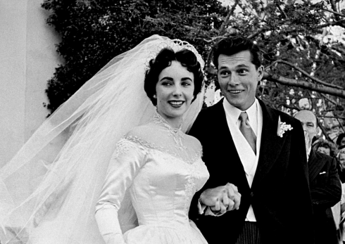 Nữ diễn viên Elizabeth Taylor mặc váy cưới làm bằng satin (trị giá 1,500USD - món quà từ hãng phim MGM) nắm tay cùng chồng là Nicky Hilton .