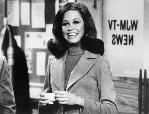 (Original Caption) Still from The Mary Tyler Moore Show showing Moore standing, smiling, inside of the WJM newsroom. Moore is shown from the waist-up, holding a cup of coffee.