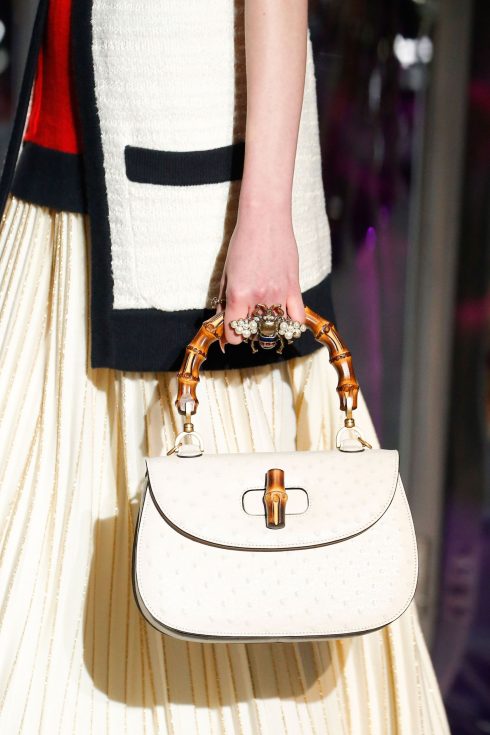 Chiếc túi với phần quai tre nổi tiếng của Gucci trên nền da đà điểu trắng và chiếc nhẫn bọ cánh cứng của Gucci.