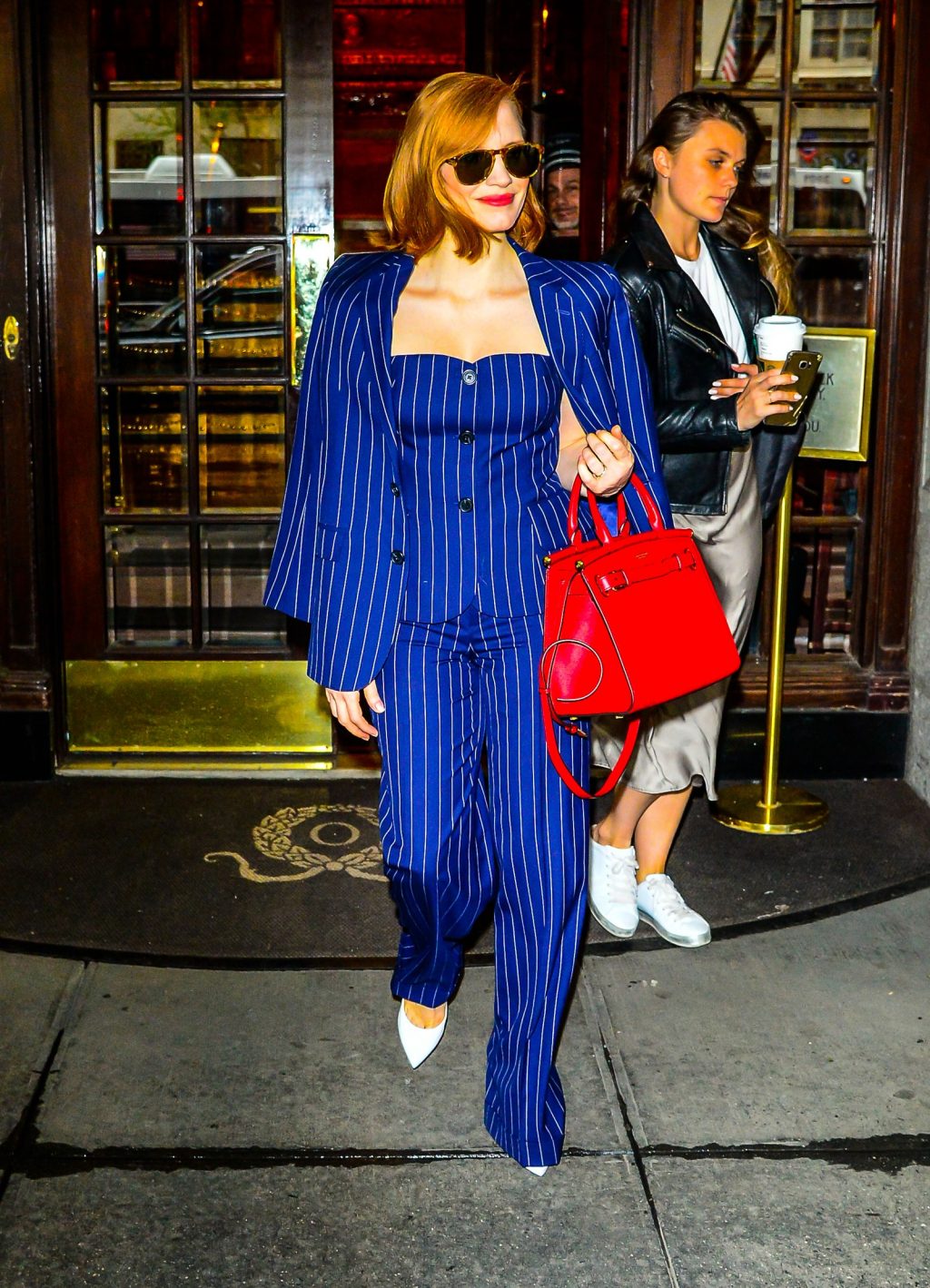 nữ diễn viên Jessica Chastain diện blazer kẻ sọc đồng bộ cùng quần âu và corset xanh cobalt của Ralp Lauren và kính mát đen, túi xách đỏ