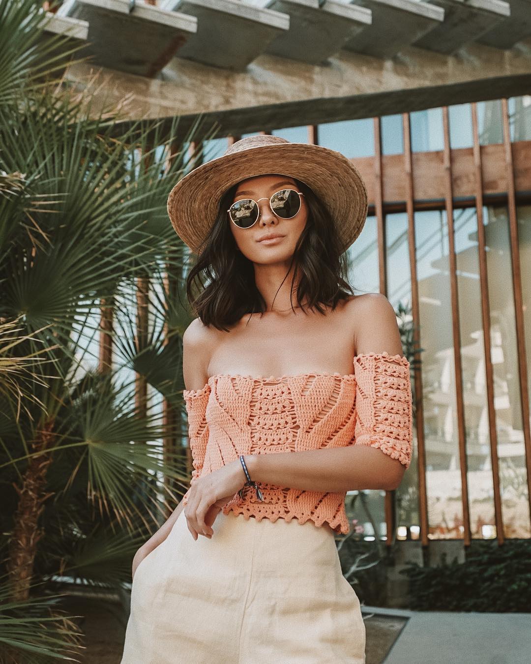 Fashionista Sophia Chang mặc áo trễ vai đan móc màu cam, đội nón rộng vành, mang kính đen
