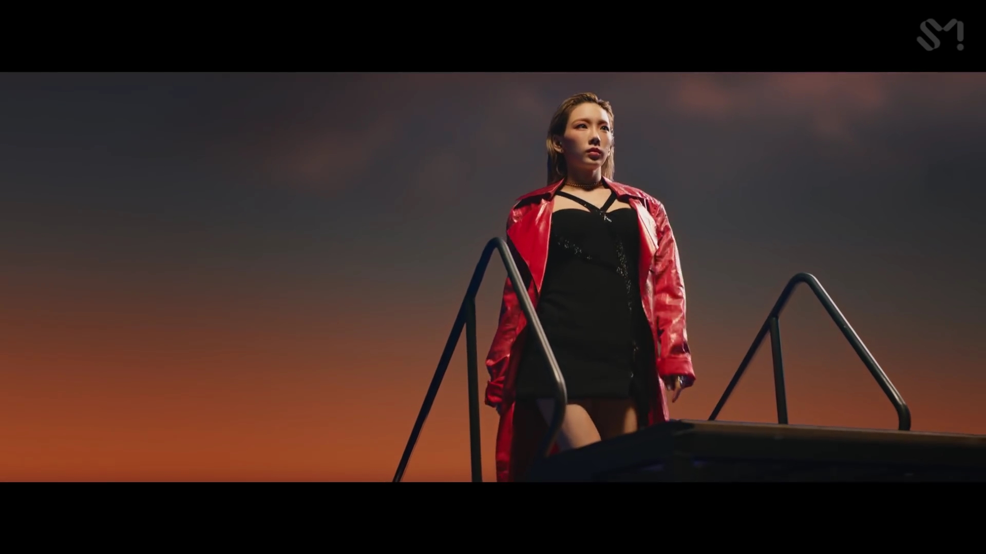Ca sĩ Taeyeon mặc đầm đen, áo khoác đỏ trong MV Spark
