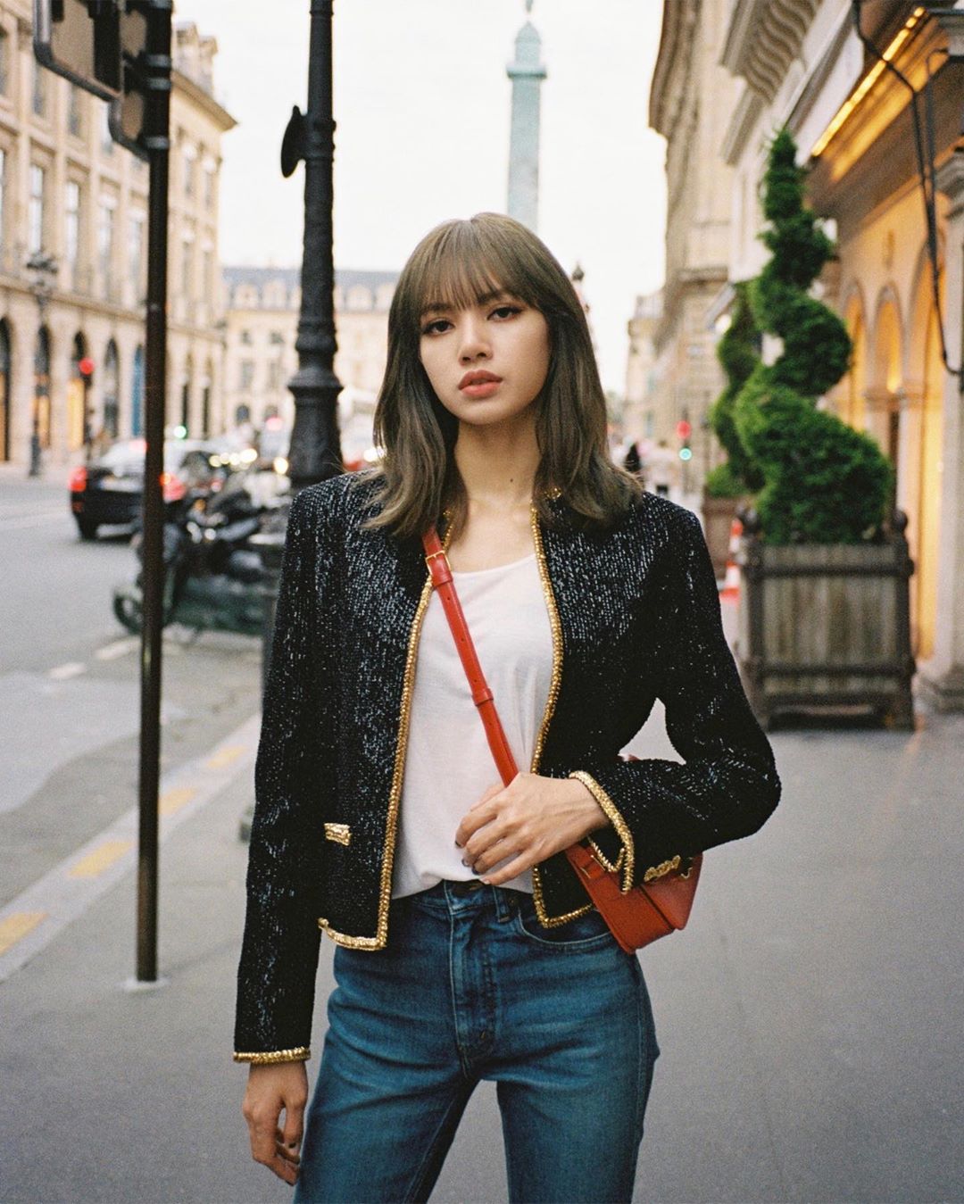 Lisa (BLACKPINK) mặc áo khoác đen kim sa, áo thun trắng, quần jeans, đeo túi xách đỏ