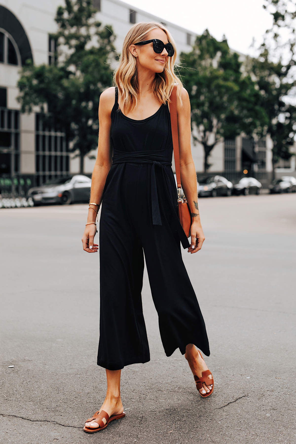 Cô gái mặc jumpsuit đen, mang dép nữ quai ngang màu nâu