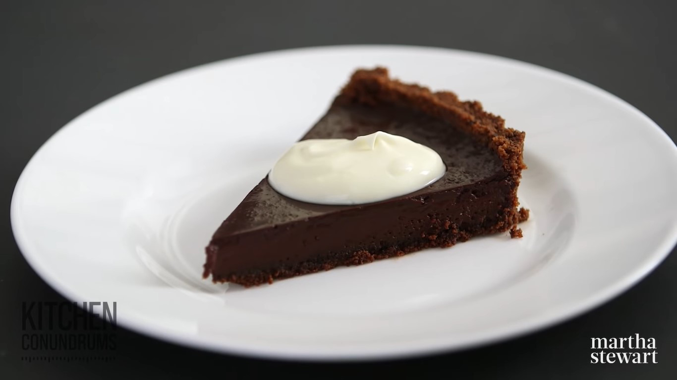Bánh tart chocolate đen có vỏ bánh bên ngoài, bên trên phủ một ít kem tươi trang trí